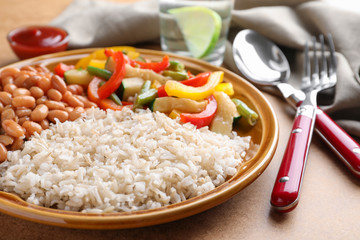 Plate of brown rice with beans and vegetables on table, closeup