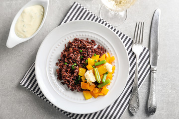Plate with delicious brown rice and vegetables on table