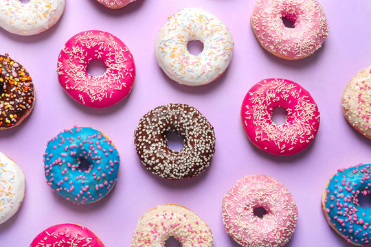 Delicious doughnuts with sprinkles on color background, top view