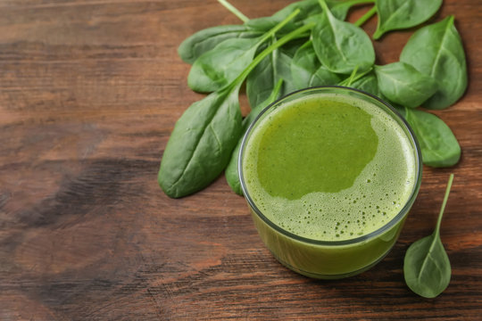 Glass with delicious detox juice and spinach on wooden background