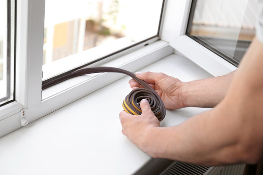 Construction Worker Putting Sealing Foam Tape On Window Indoors