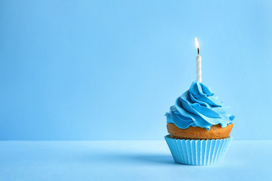 Delicious birthday cupcake with candle on color background