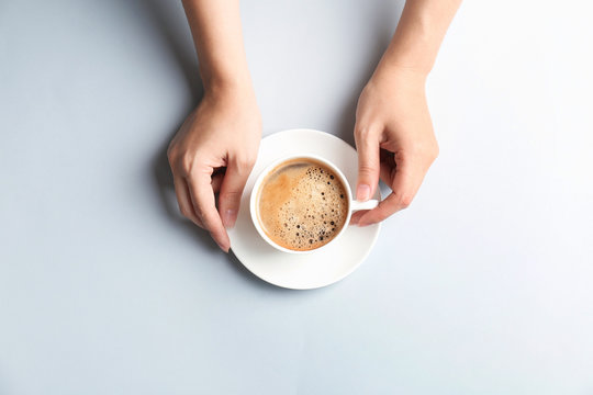 Fototapeta Young woman with cup of delicious hot coffee on light background, top view