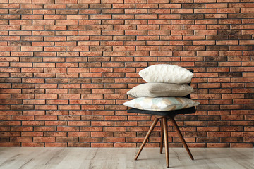 Stack of pillows on chair near brick wall