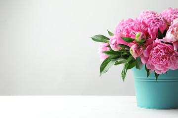 Bucket with beautiful peony flowers on table against light background