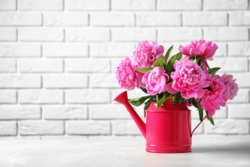 Watering can with beautiful peony flowers on table against brick wall