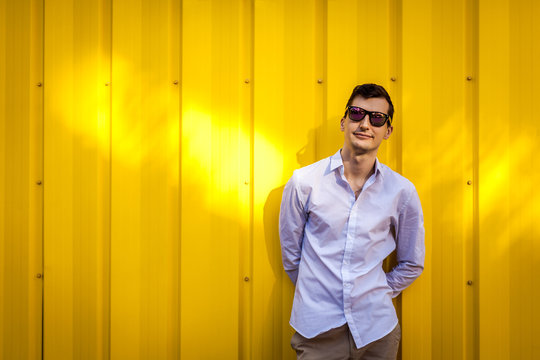 Young handsome man wearing stylish summer outfir against yellow wall outdoors. Hipster guy