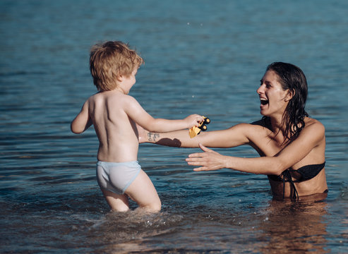 Cute child boy play with mom in sea, ocean. Mom and kid with smiling faces spend time together in sea on sunny day. Motherhood concept. Mother swimming in sea and looks at child.