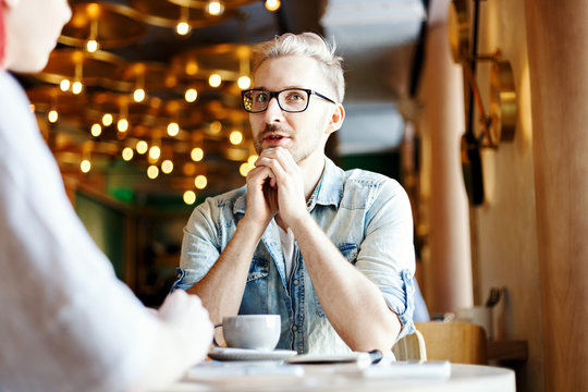 Young Man Talking To His Unrecognizable Female Friend In Cafe. Guy Telling Story Or Giving Interview Over Cup Of Coffee.