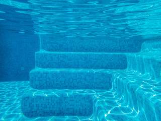 Fototapeta na wymiar underwater image of swimming pool steps with sunlight causing patterns on the tiled blue steps