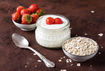 White yogurt in glass bowl with spoon and starwberries on rustic background.