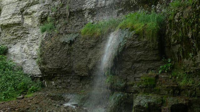 shot backing up from a long thin waterfall as it pours down the side of a rocky and mossy cliff