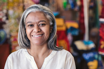 Smiling mature woman standing in her colorful clothing shop