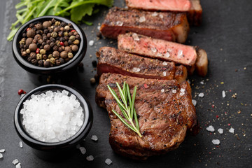 Closeup ready to eat steak new York beef breeds of black Angus with herbs, garlic and butter on a stone Board. The finished dish for dinner on a dark stone background. Top view