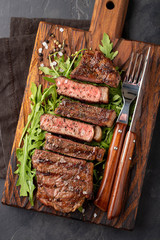 Closeup ready to eat steak new York beef breeds of black Angus with herbs, garlic and butter on a wooden Board. The finished dish for dinner on a dark stone background. Top view