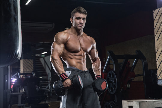 Handsome young fit muscular caucasian man of model appearance workout training in the gym gaining weight pumping up muscle and poses fitness and bodybuilding sport nutrition concept