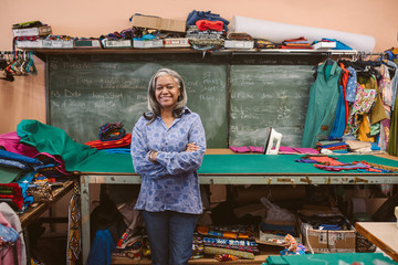Smiling mature seamstress standing by her shop workbench