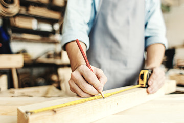 Hands of unrecognizable carpenter measuring wood plank with tape measure and making pencil marks