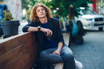  Red haired hipster man sitting on bench with coffe to go