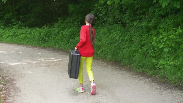 girl, walks through the woods with a heavy black suitcase. 4k, slow-motion shooting, steadicam shot.
