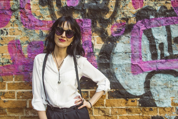 Stylish young woman on graffiti background. Portrait of a fashionable female in sunglasses.