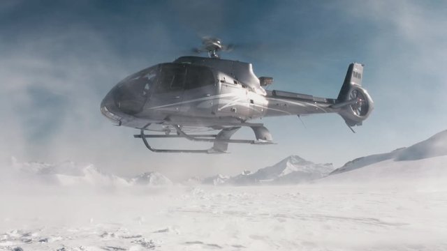 Black helicopter taking off from an alpine mountain with snow blowing in the wind