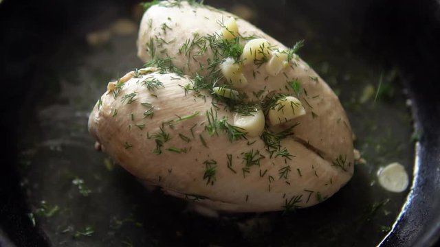 Close-up someone sprinkles meat seasoning, cooking chicken breast with garlic and dill on a cast-iron frying pan, slow motion.