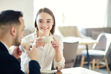 Young business people, man and woman, having friendly talk in cafe. Businessman and businesswoman enjoying networking coffee meeting. Focus on smiling young woman holding cup of coffee