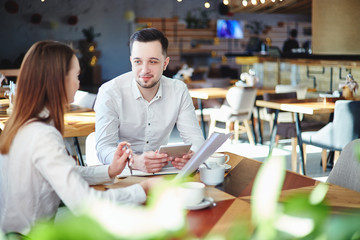Business partners planning project at cafe. Businesswoman with documents in her hands and businessman with tablet computer sitting at table and talking