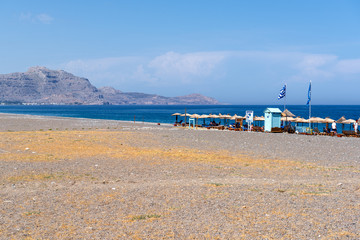 Fototapeta premium Kalathos beach located near Kalathos village. Pebble and sandy beach with many sun beds with umbrellas. Rhodes island, Greece
