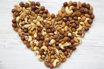 Pattern of nuts in heart form. Cashew, hazelnuts, walnuts, almonds on white wooden background, top view. Flat lay.