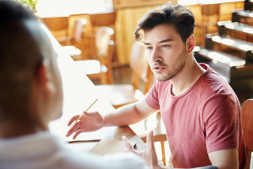 Handsome college student discussing ideas with his friend while working on project together