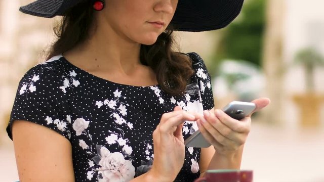 Beautiful lady in hat sitting at street cafe, scrolling smartphone application