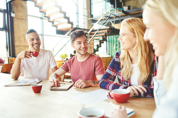 Group of cheerful young coworkers having fun at coffee break - chatting over coffee and laughing