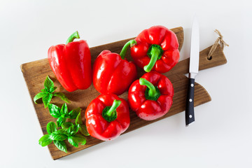a group of red ripe organic peppers and fresh basil leaves on a cutting board and a knife.