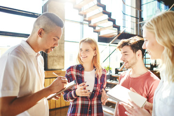 Young diverse startup team brainstorming. Four cheerful friends discussing ideas and writing them down in notepads