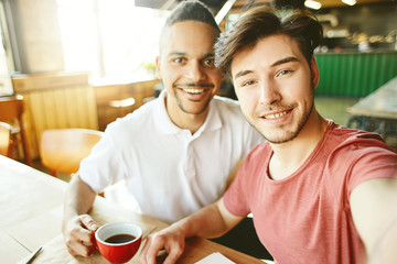 Two cheerful adult students taking selfie in college cafeteria and smiling