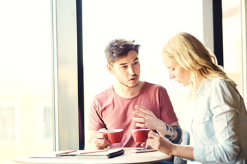Obraz premium Young man talking something to his girlfriend who texting on her smartphone. Couple having coffee together in cafe
