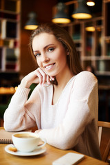 Beautiful confident businesswoman having cup of coffee while sitting at table in cafe and smiling at camera