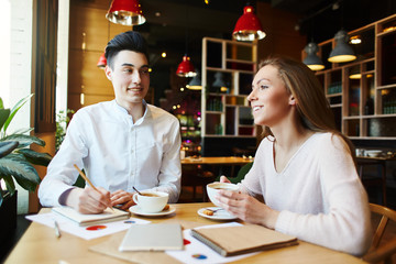 Young woman and man sitting at cafe table with coffee cups and planning business strategy