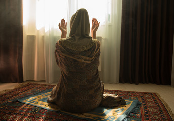 Muslim woman praying for Allah muslim god at room near window. Hands of muslim woman on the carpet...