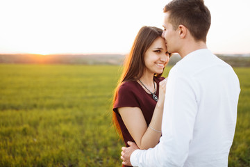young, happy, loving couple, at sunset, standing in a green field, against the sky, in the arms, and enjoying each other, advertising and inserting text