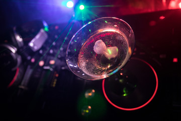 Glass with martini with olive inside on dj controller in night club. Dj Console with club drink at music party in nightclub with disco lights. Close up view
