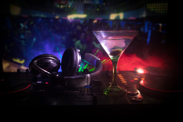 Glass with martini with olive inside on dj controller in night club. Dj Console with club drink at music party in nightclub with disco lights. Close up view