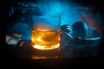 Glass with whisky with ice cube inside on dj controller at nightclub. Dj Console with club drink at...