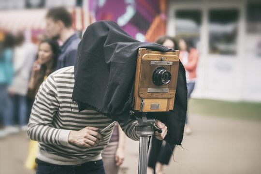 Photographer with antiquity vintage wooden camera under dark cloth cape photographing passers - old classical action, rarity concept