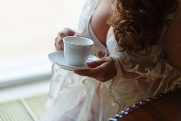 Close-up of a girl's hand in a boudoir dress drinking tea or coffee. The morning of the bride at the hotel before the wedding in the Church.