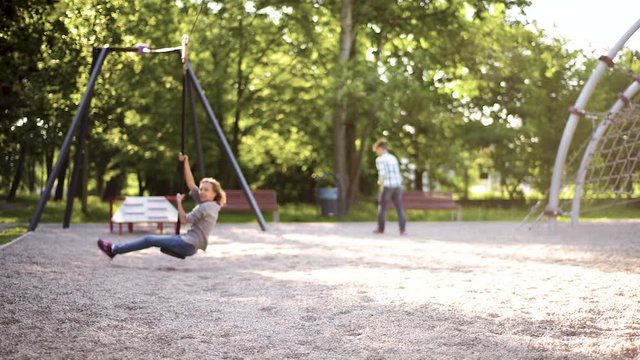Children having fun is riding zipline. Cute girl and teen boy moving on zip line at playground - outdoors.