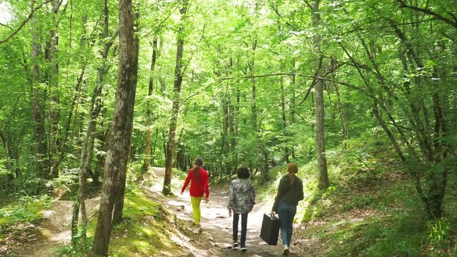 woman, girl and boy, walks through the woods with a heavy black suitcase. 4k, slow-motion shooting, steadicam shot.