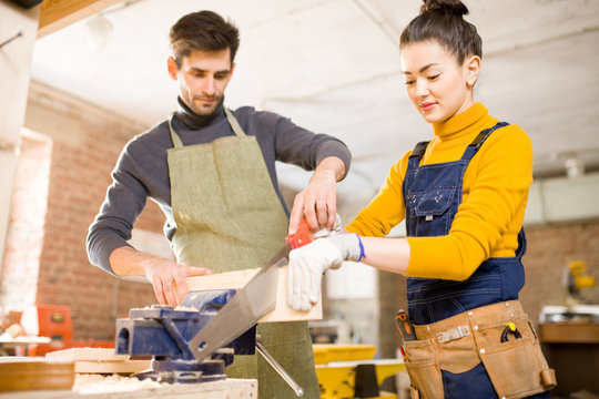 Portrait Of Smiling  Female Artisan Cutting Wood While Working  With Male Colleague In Modern Furniture Manufactory, Copy Space